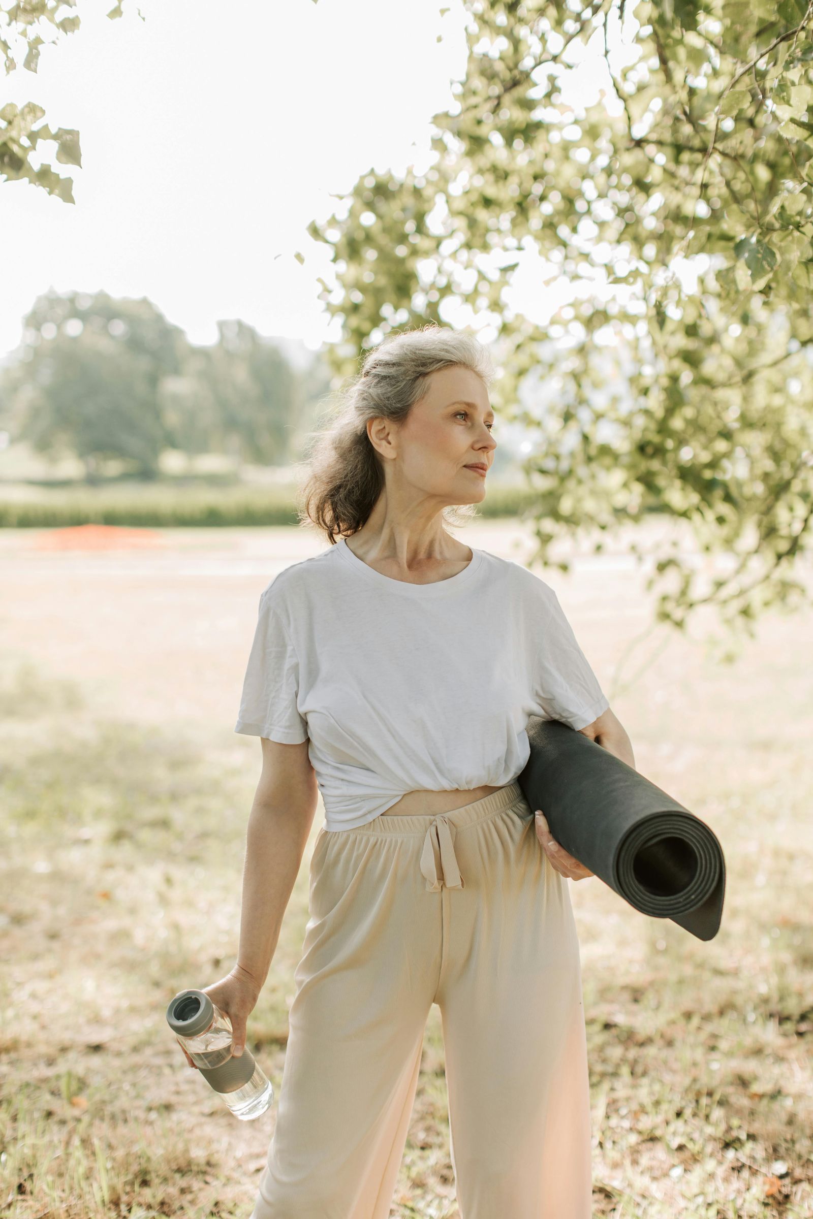 Femme senior souriante en tenue de yoga avec son tapis, prête pour une séance d'activité physique douce en plein air
