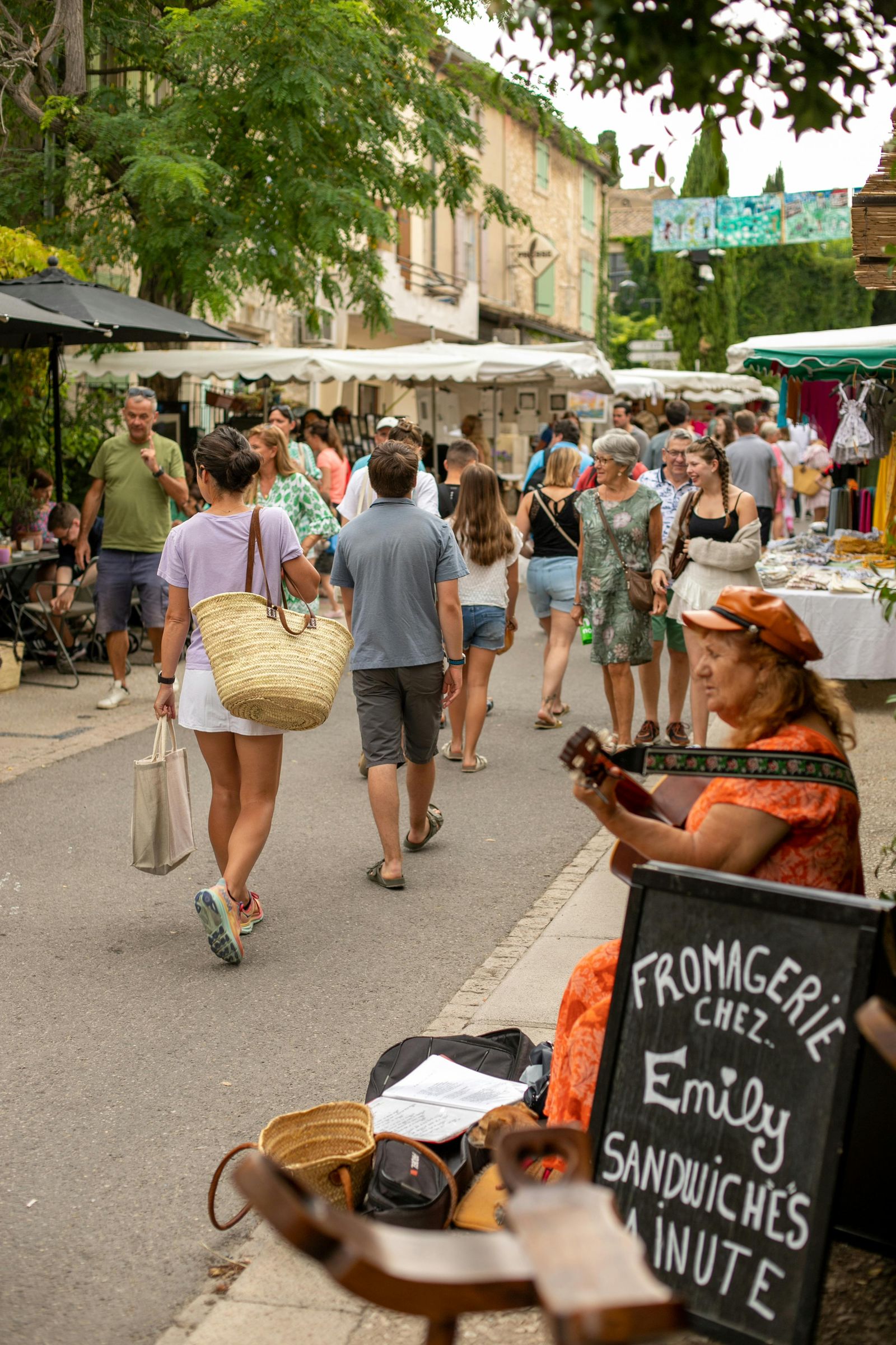 Marché provençal animé avec étals, panier en osier et musicienne au premier plan