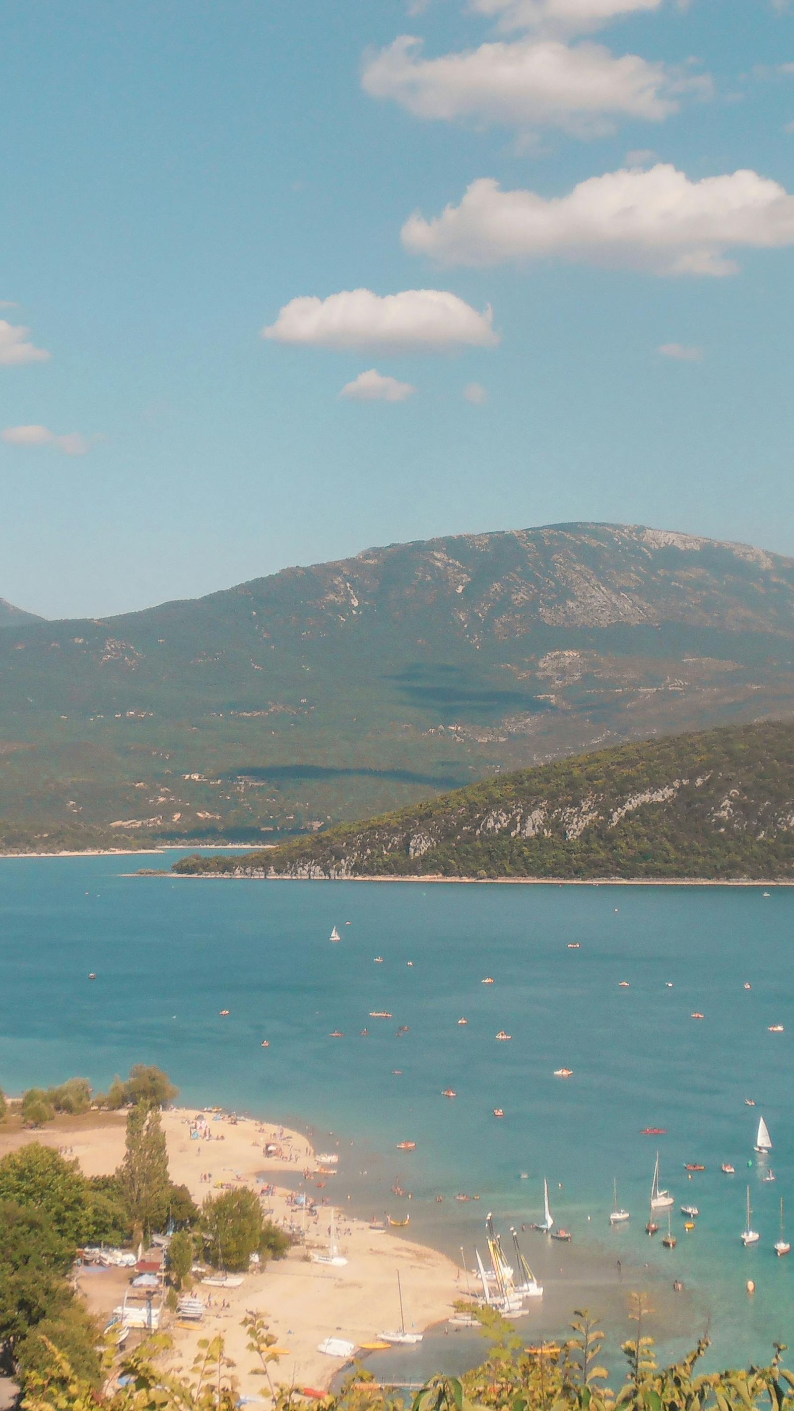 Plage du lac de Sainte-Croix avec voiliers et pédalos, vue sur les collines provençales